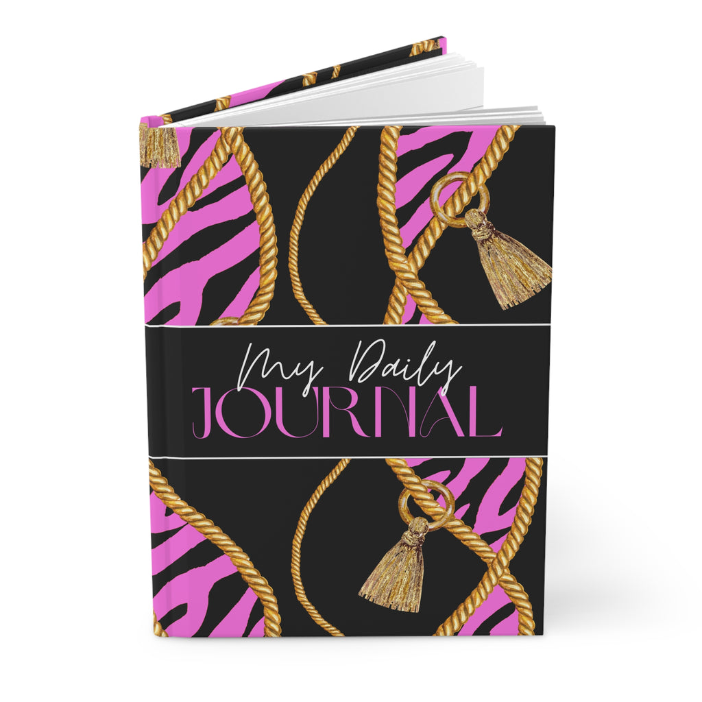 A hardcover daily journal with a black cover featuring pink zebra stripes, gold rope patterns, and tassels, with a central black band reading 'My Daily JOURNAL' in white and pink script.