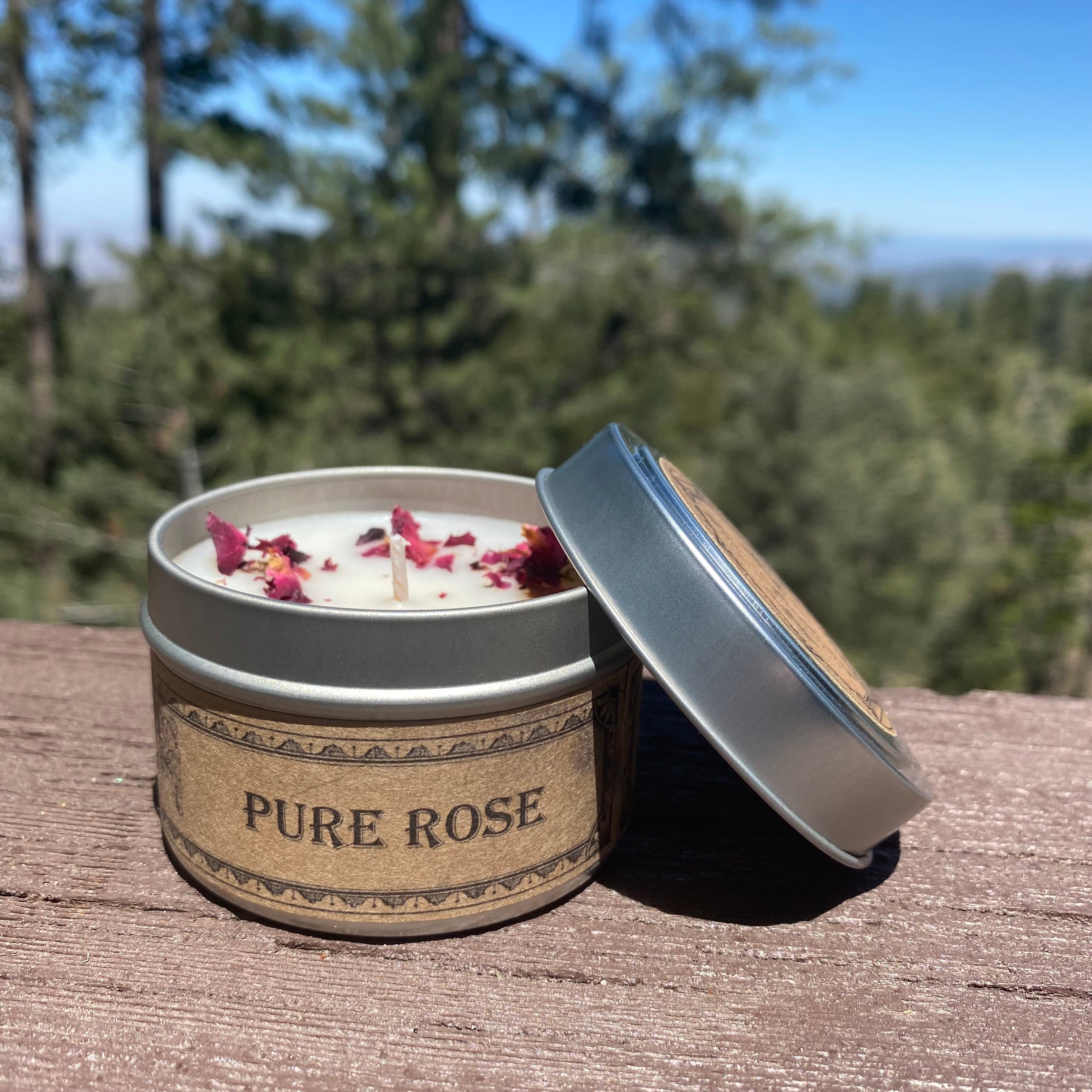Candle labeled 'Pure Rose' with a natural lid on a wooden surface with a forest background