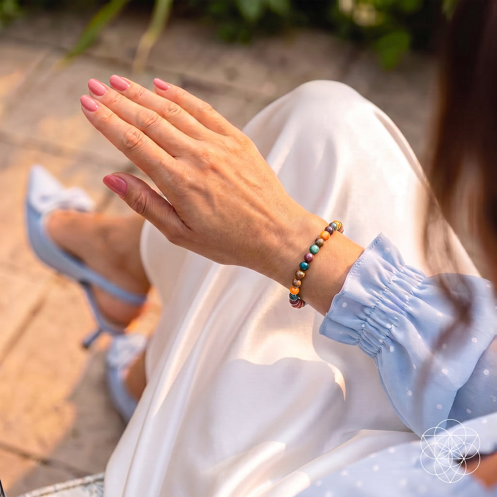 A close-up lifestyle shot of a woman's hand wearing a beaded bracelet with colorful round beads, paired with a light blue and white polka dot blouse and white pants.