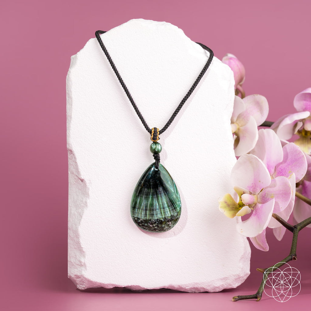 Green pendant necklace on a white stone with pink flowers on a pink background