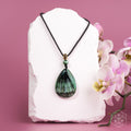 Green pendant necklace on a white stone with pink flowers on a pink background