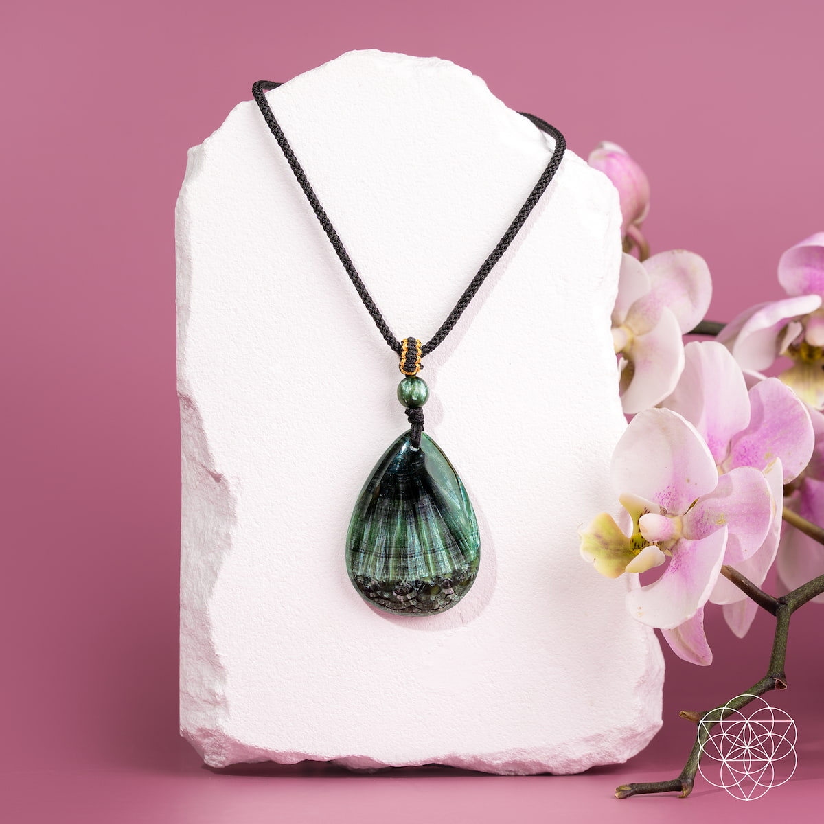 Green pendant necklace on a white stone with pink flowers on a pink background