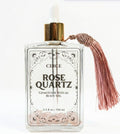 Circe Rose Quartz body oil bottle with a tassel on a white background