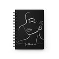 A black spiral-bound notebook with a minimalist white line art illustration of a woman's face and the word 'selfcare' written in script near the bottom, shown on a plain white background.