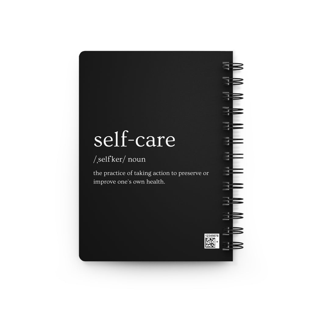 A black spiral-bound notebook featuring a dictionary-style definition of 'self-care' printed in white text on the front cover, shown against a plain white background.