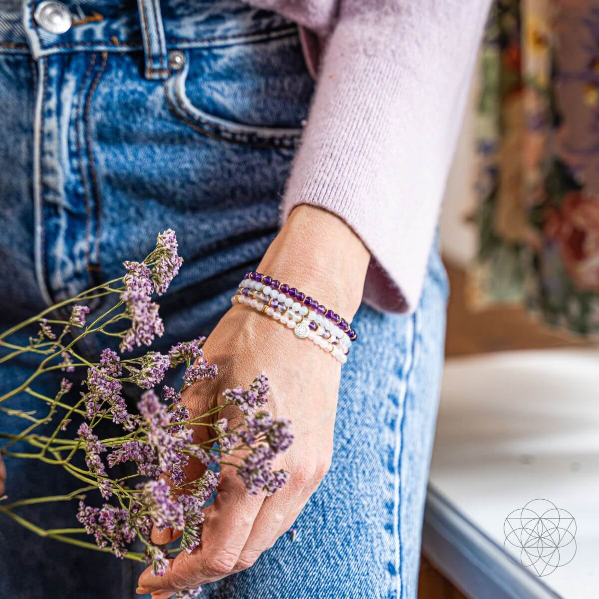 Person holding a branch of purple flowers with bracelets on a blurred background