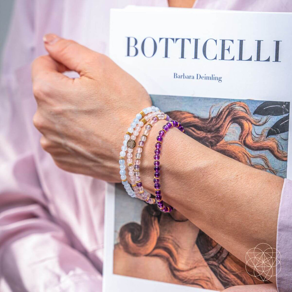 Person wearing multiple bracelets on wrist with 'BOTTICELLI' book in background