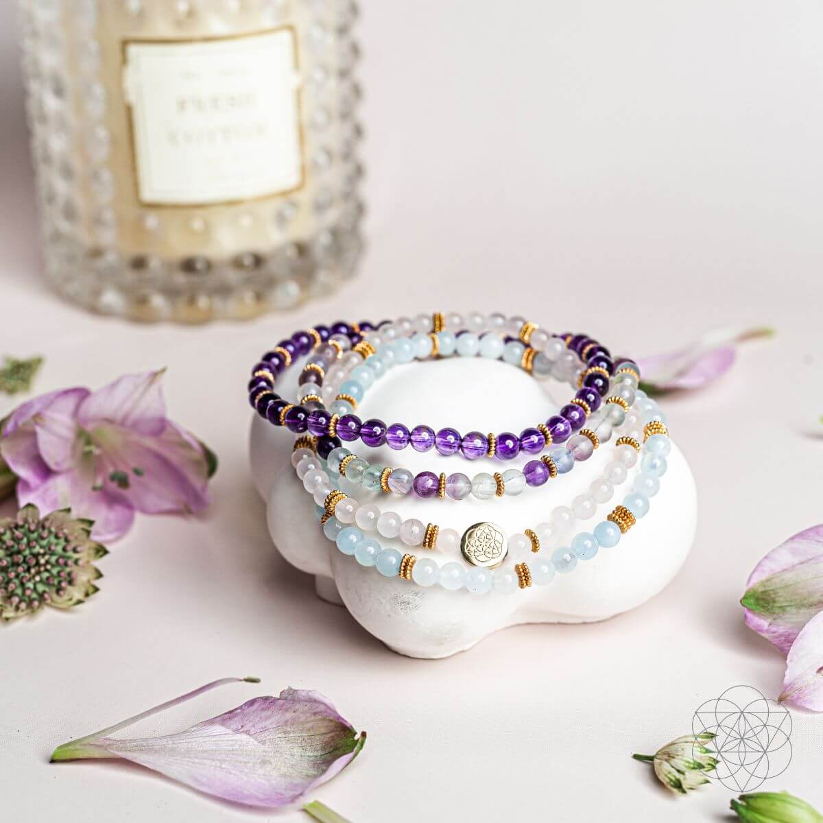 Stack of beaded bracelets on a white dish with flowers and a candle in the background