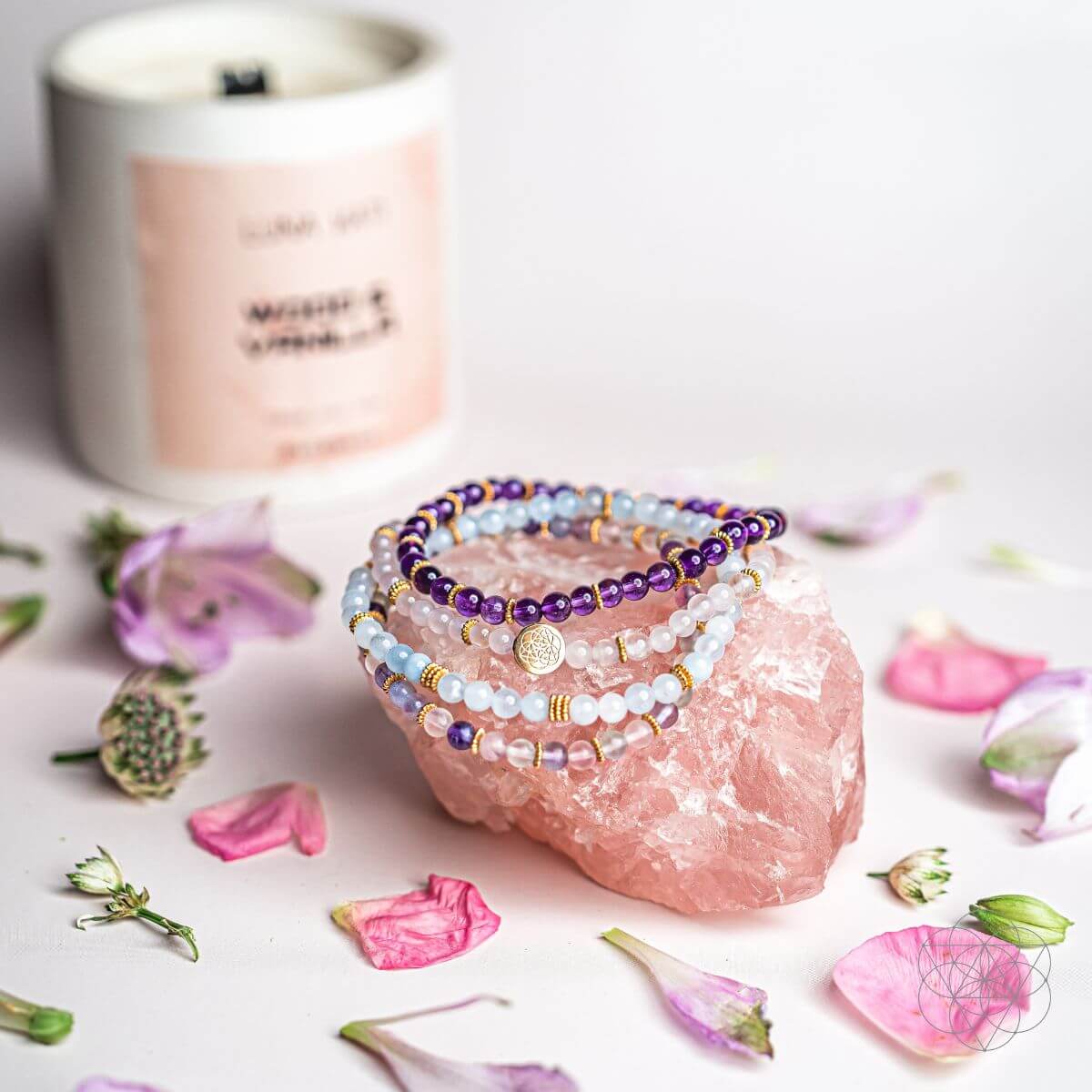 Stack of beaded bracelets on a pink crystal with flowers and a candle in the background
