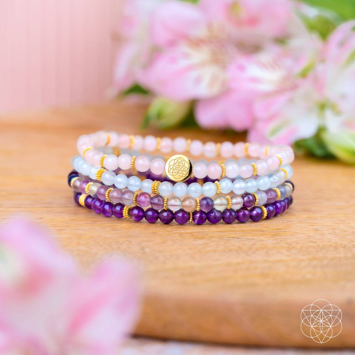 Stack of beaded bracelets on a wooden surface with flowers in the background