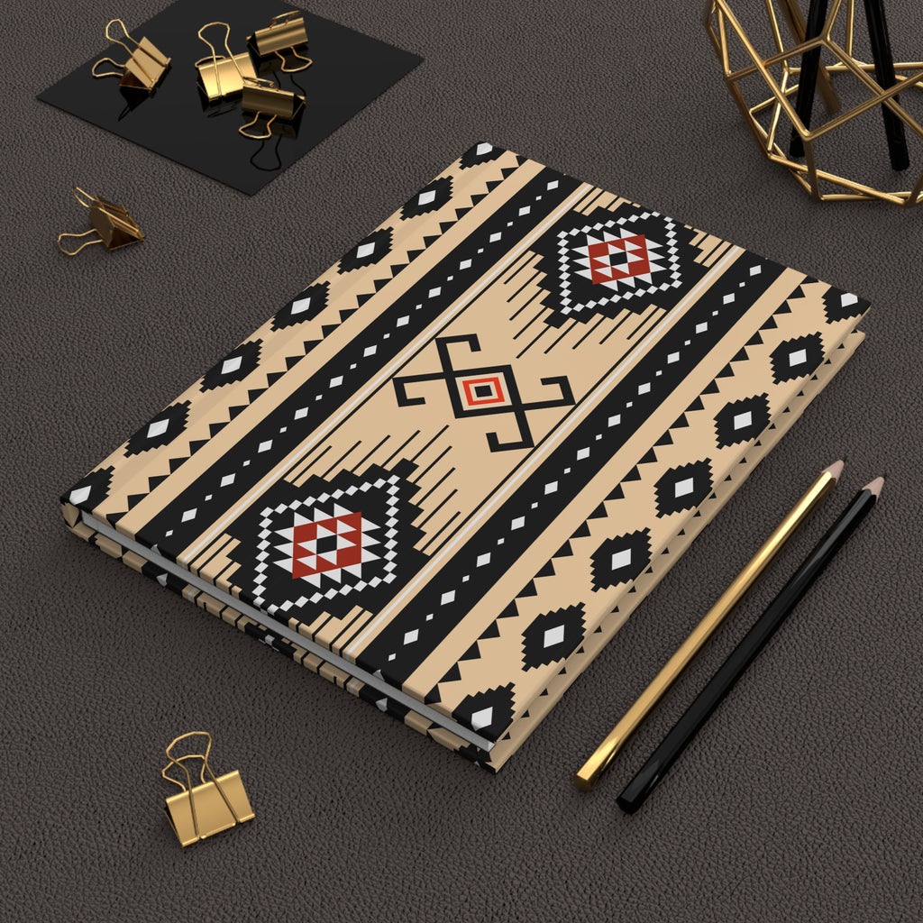A notebook with a Southwestern geometric pattern in beige, black, and red, styled on a dark textured surface with gold and black pencils, binder clips, and a gold geometric decor piece.