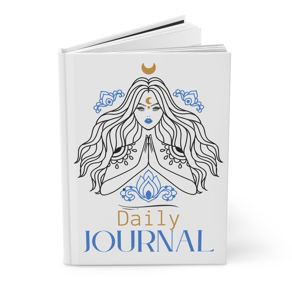 A white hardcover daily journal shown open at a slight angle, featuring a line-art illustration of a woman with long flowing hair, blue decorative motifs, a gold crescent moon, and the text 'Daily JOURNAL' on the cover.