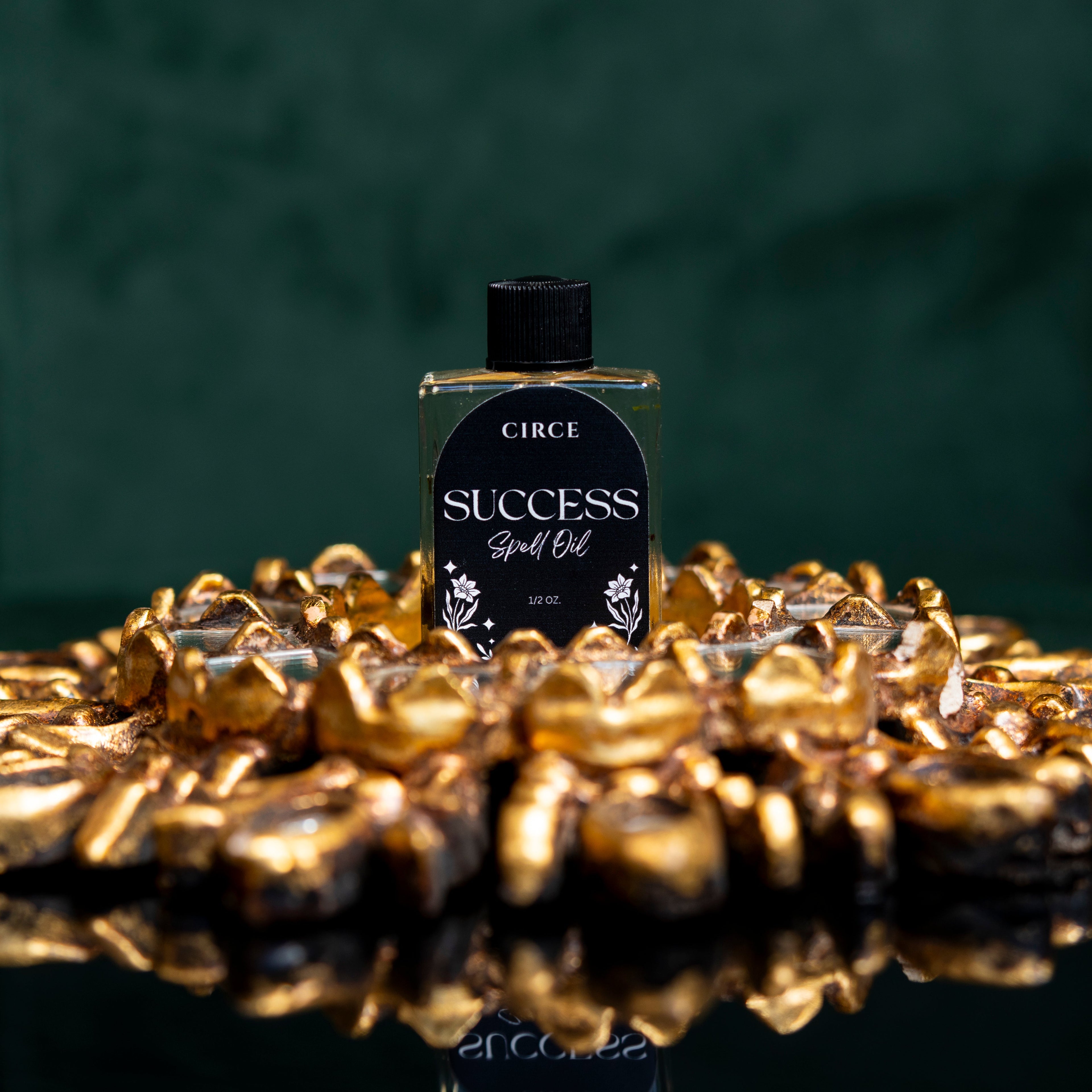 Bottle of Circe Success Spell Oil surrounded by gold coins on a reflective surface with a dark background