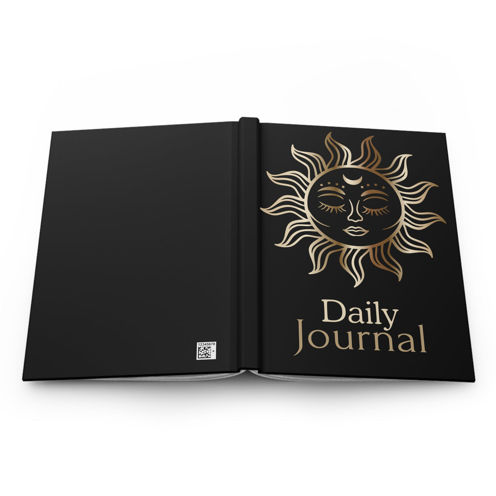 An open black hardcover daily journal with a gold sun face illustration and the words 'Daily Journal' on the right page, shown against a plain white background.