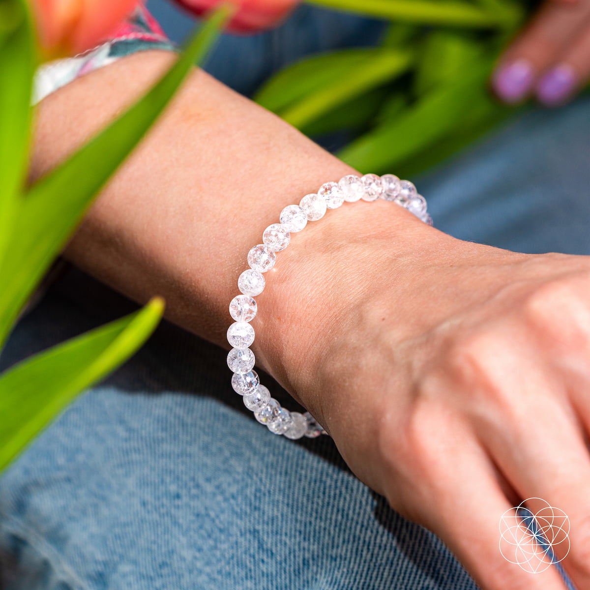 Close-up of a wrist wearing a clear beaded bracelet with a blurred background of green leaves and a person's hand.