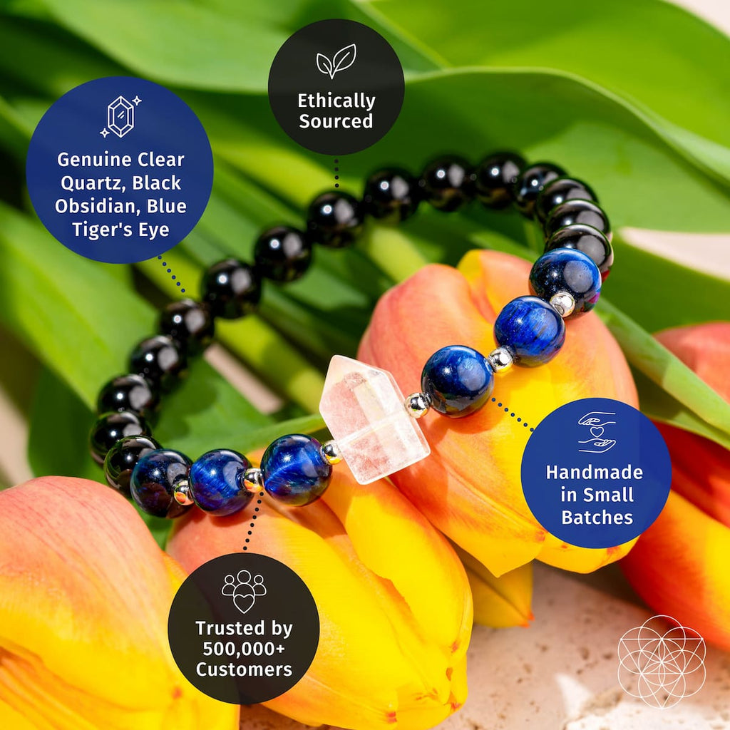 A beaded bracelet arranged on yellow and orange flowers with green leaves. The bracelet features glossy black beads, deep blue lapis lazuli-style beads, a clear faceted quartz crystal, and small silver spacer beads.