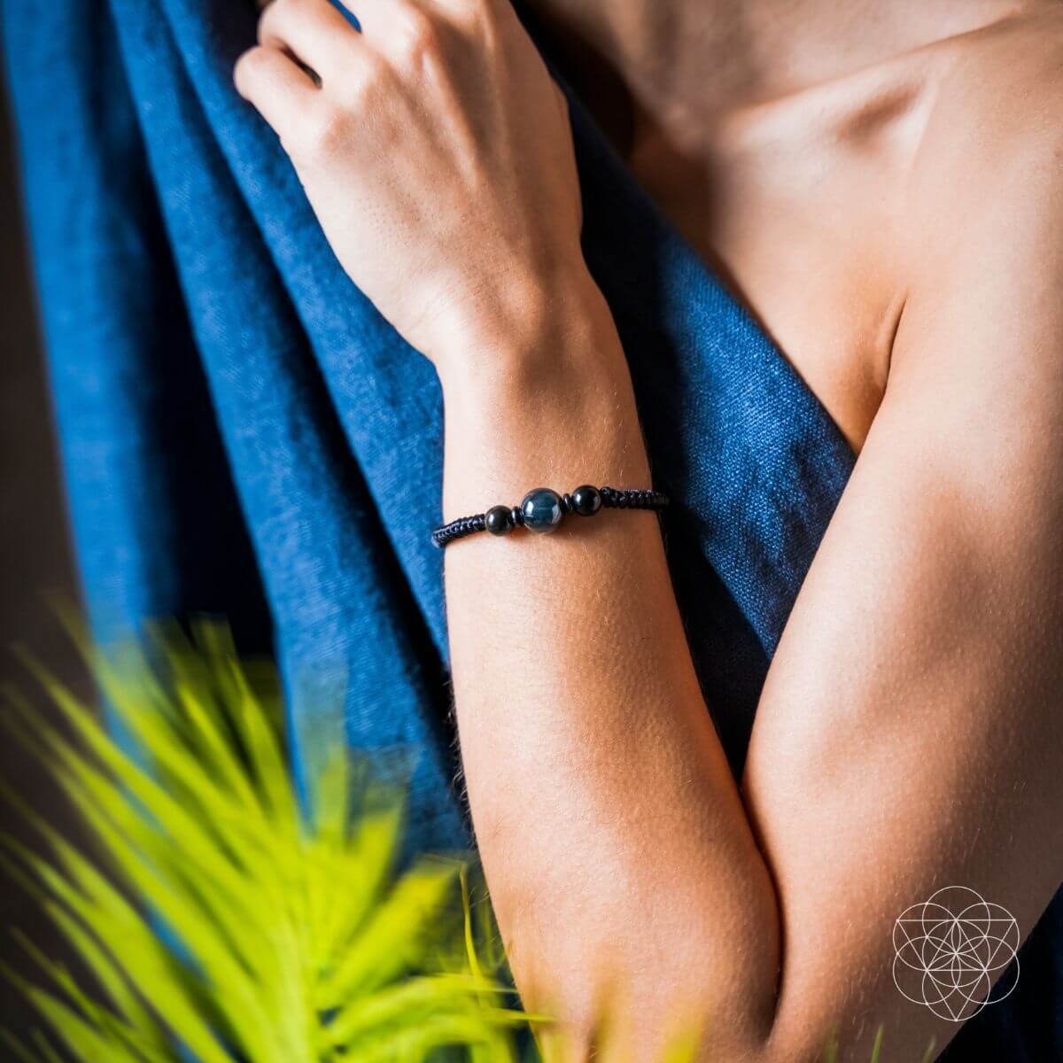 Person wearing a black beaded bracelet with a blue towel and green plant in the background