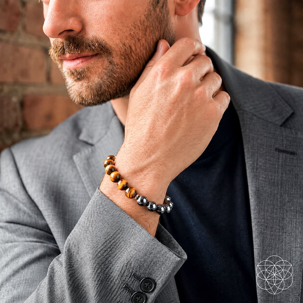 Man wearing a gray suit with a beaded bracelet, against a brick wall background.