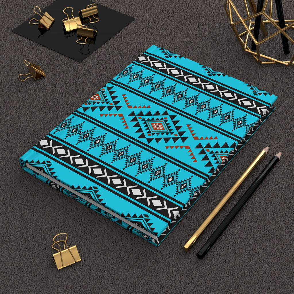 A notebook with a vibrant turquoise, black, and white geometric patterned cover, styled on a dark textured surface with gold and black office accessories.