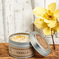 Vanilla scented candle in a tin with a yellow flower on a wooden surface