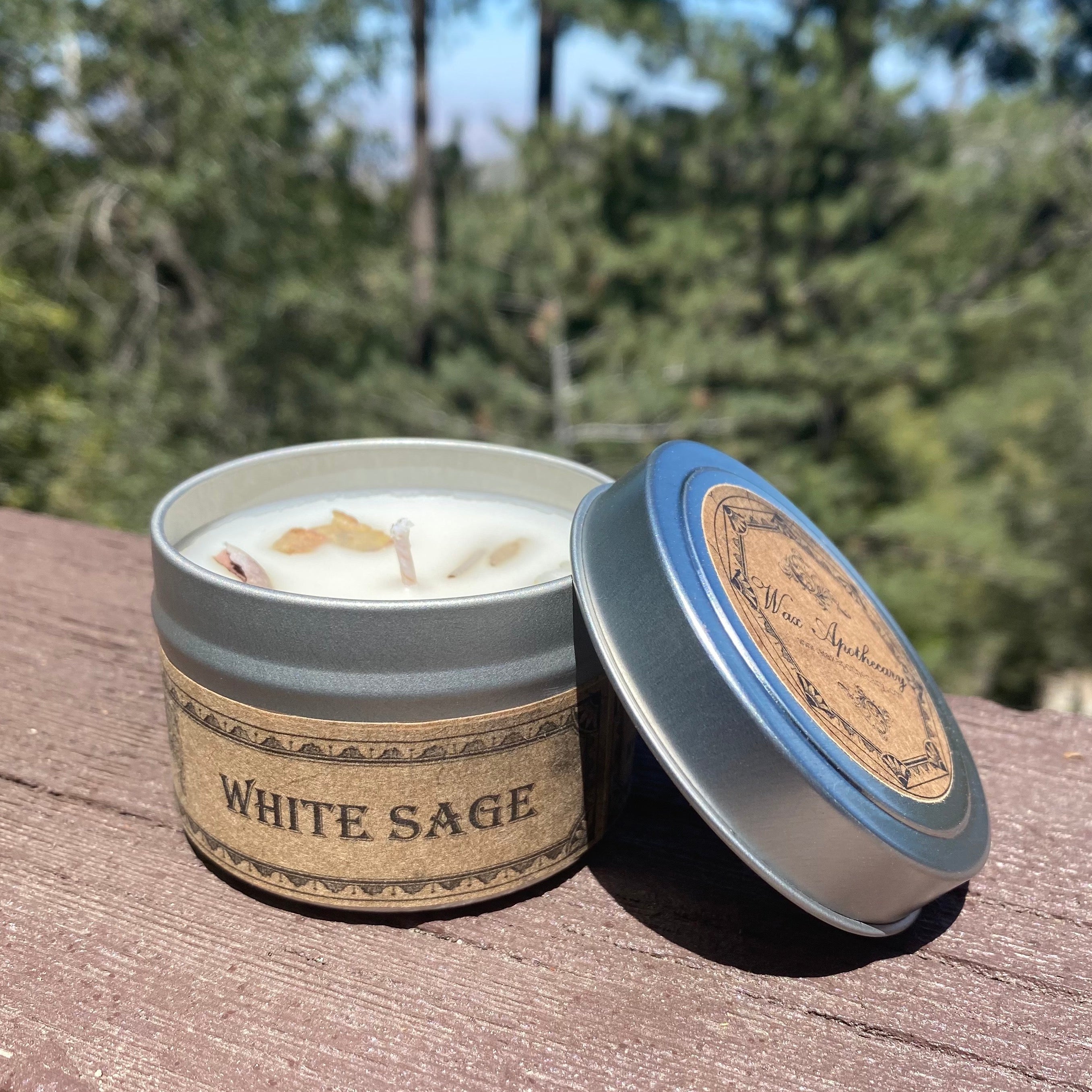 White Sage candle in a tin with a wooden lid on a wooden surface with a blurred natural background