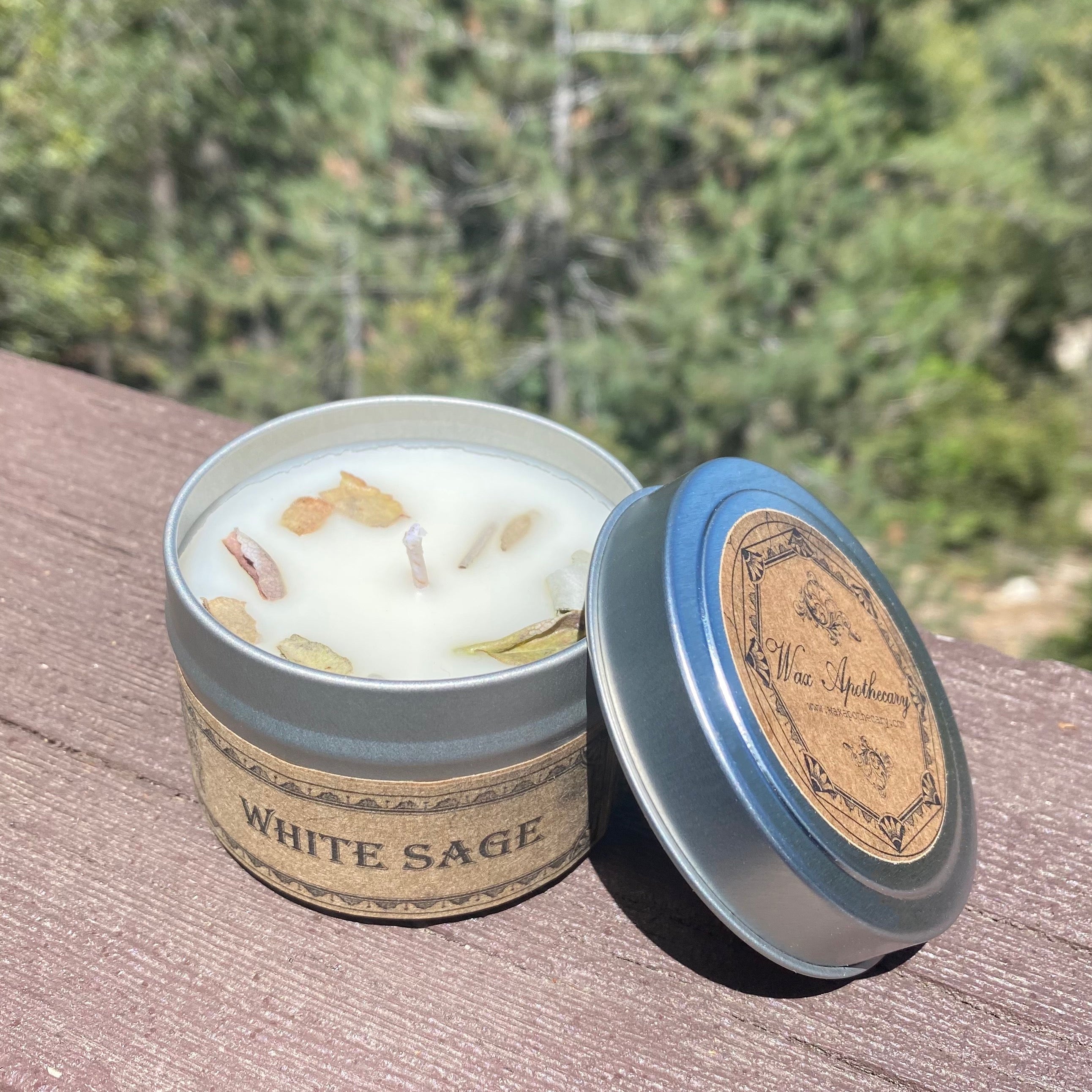 White sage candle in a tin with a wooden lid on a wooden surface with a blurred natural background