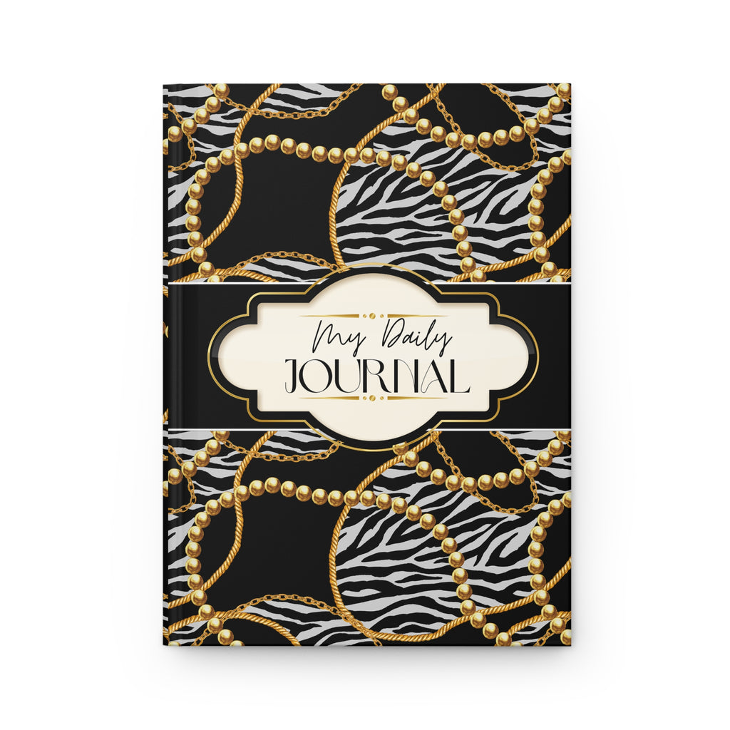 A hardcover daily journal with a black and white zebra print cover patterned with gold chains and pearl-like circles, featuring a cream-colored central label with the text 'My Daily JOURNAL'.