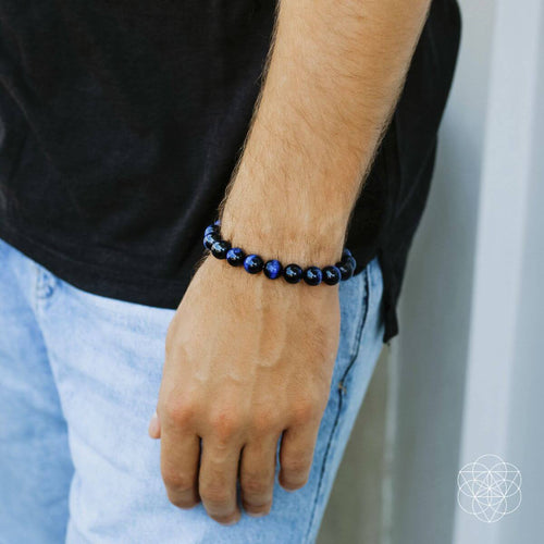 Person wearing a black beaded bracelet on a neutral background
