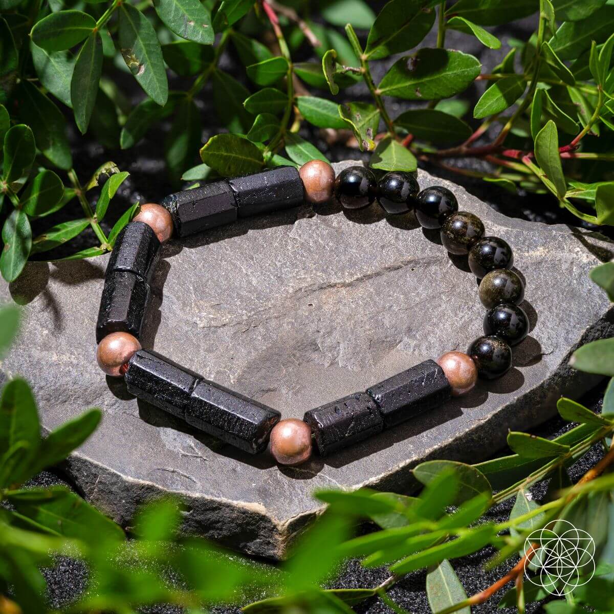 Black and brown beaded bracelet on a stone surface with green leaves in the background