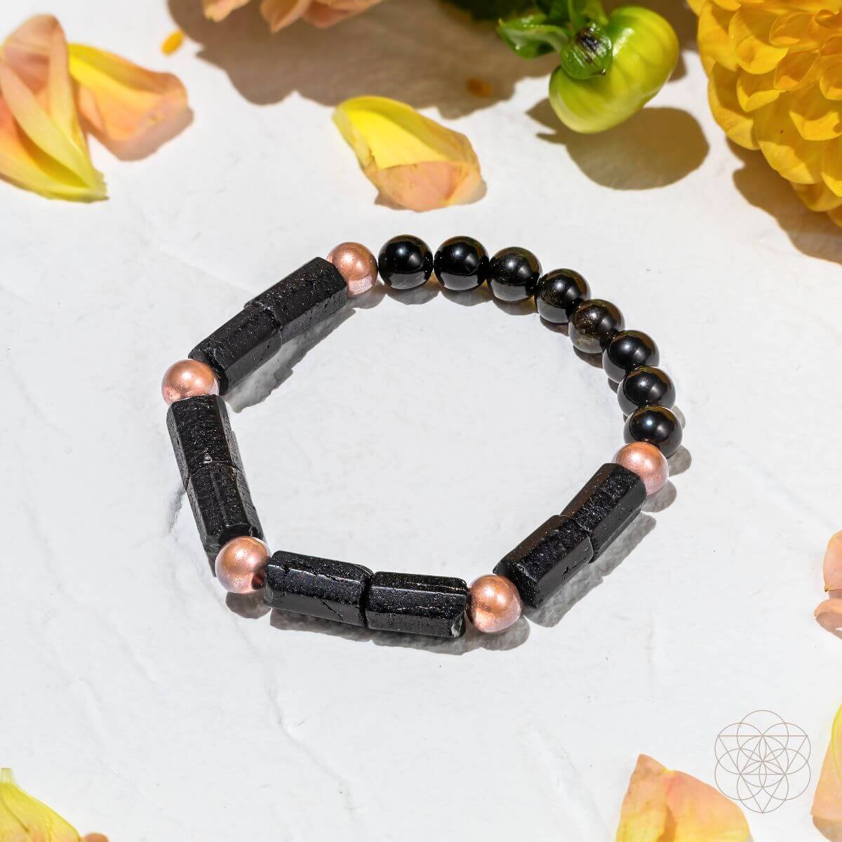Black beaded bracelet with pink accents on a white background with flowers
