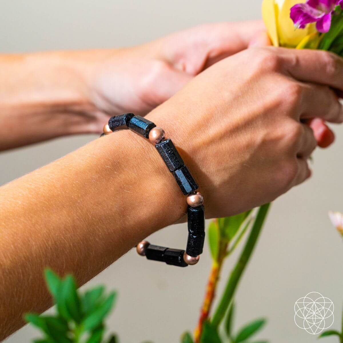 Person wearing a black beaded bracelet holding flowers against a neutral background