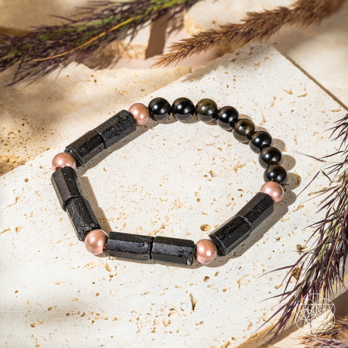 Bracelet with black and pink beads on a textured surface with dried grasses.