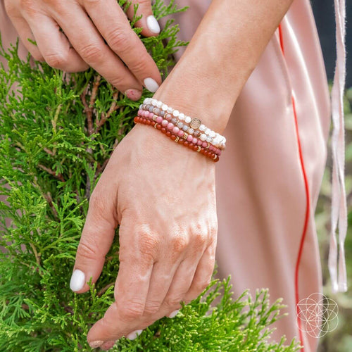 Close-up of a hand wearing multiple beaded bracelets on a green leafy background