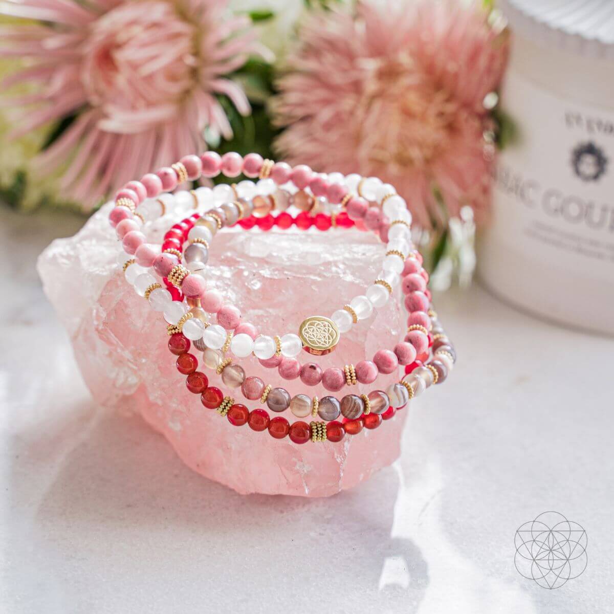 Stack of beaded bracelets on a pink crystal with pink flowers in the background