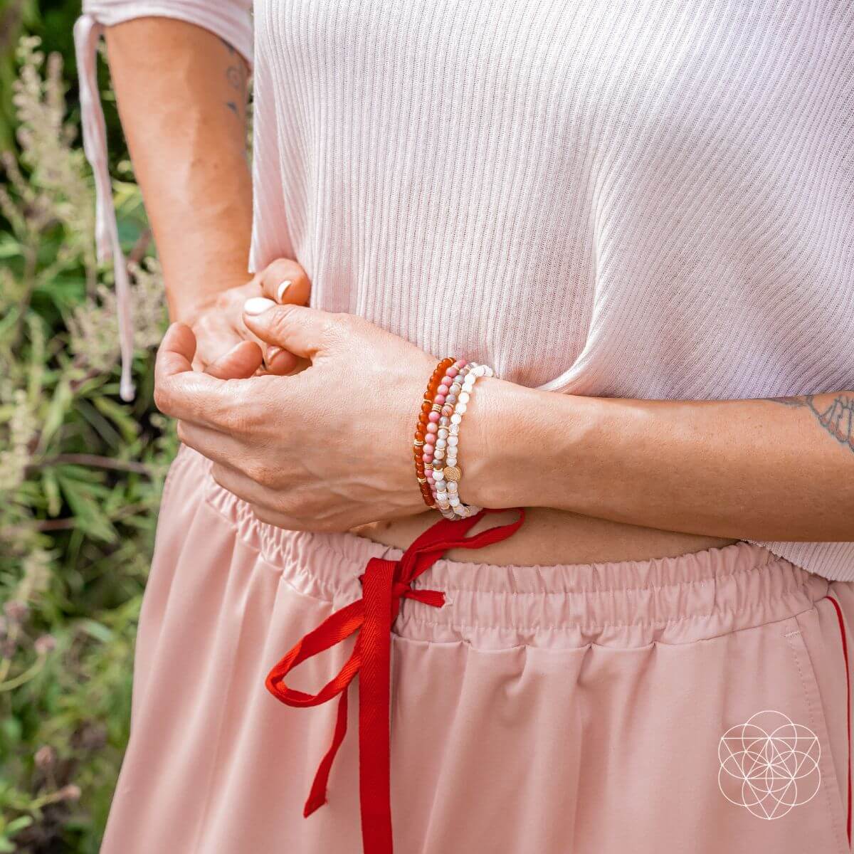 Person wearing a white top and pink pants with a red ribbon, holding hands.