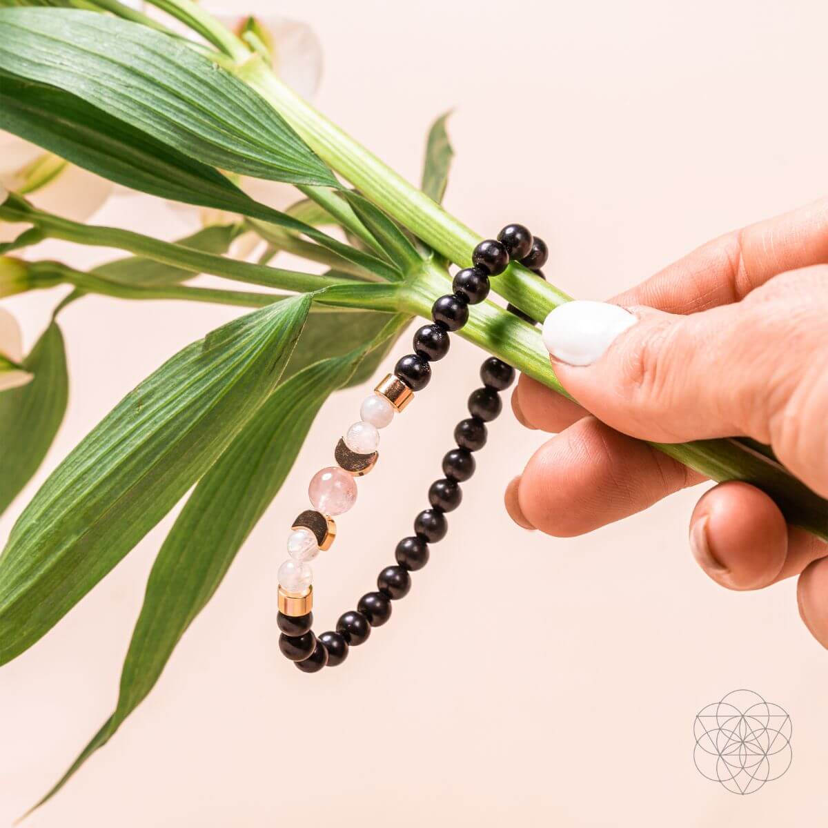 Hand holding a black beaded bracelet with a plant leaf on a beige background