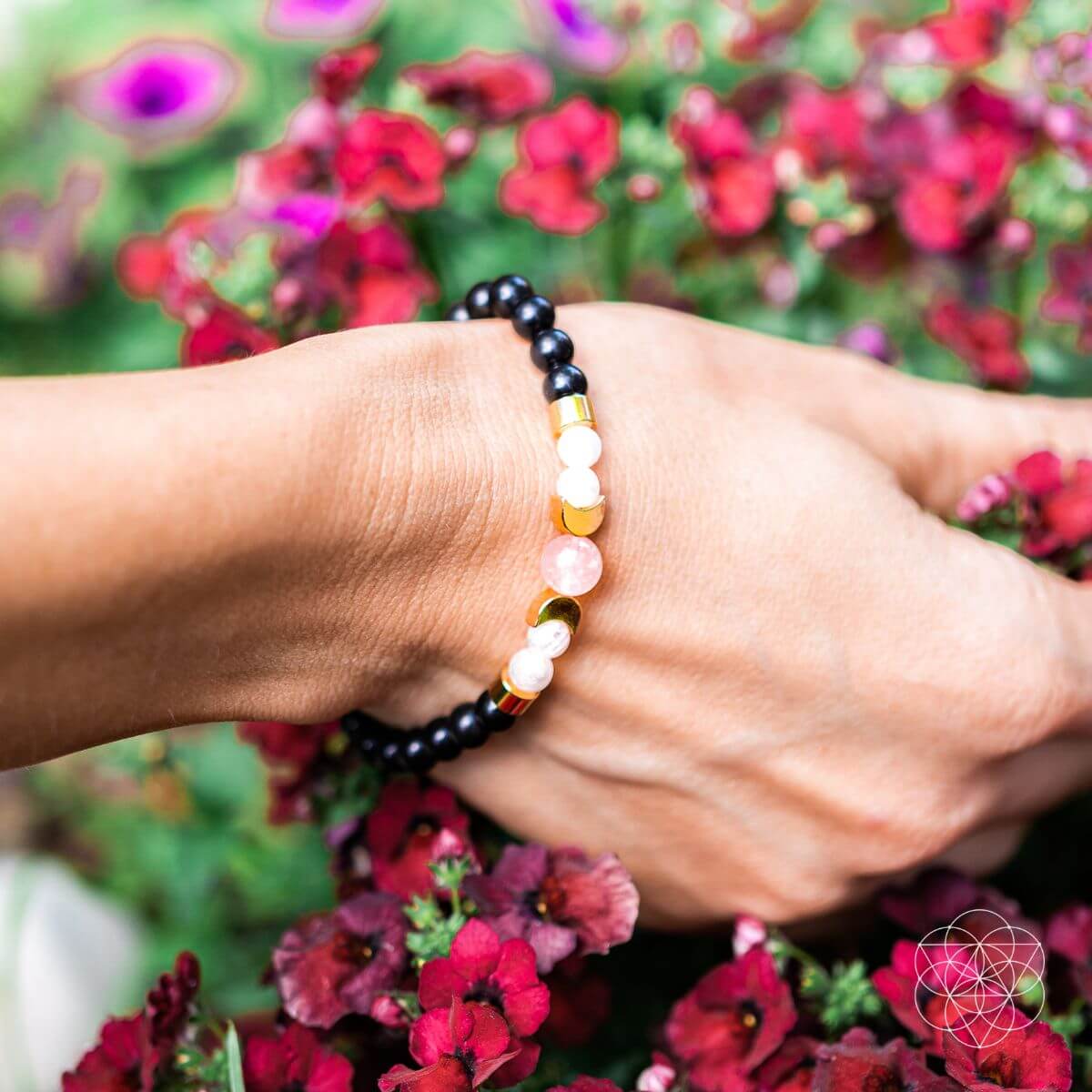 Hand wearing a beaded bracelet with flowers in the background