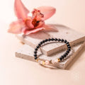Black beaded bracelet with gold accents on a stone surface with a pink flower in the background