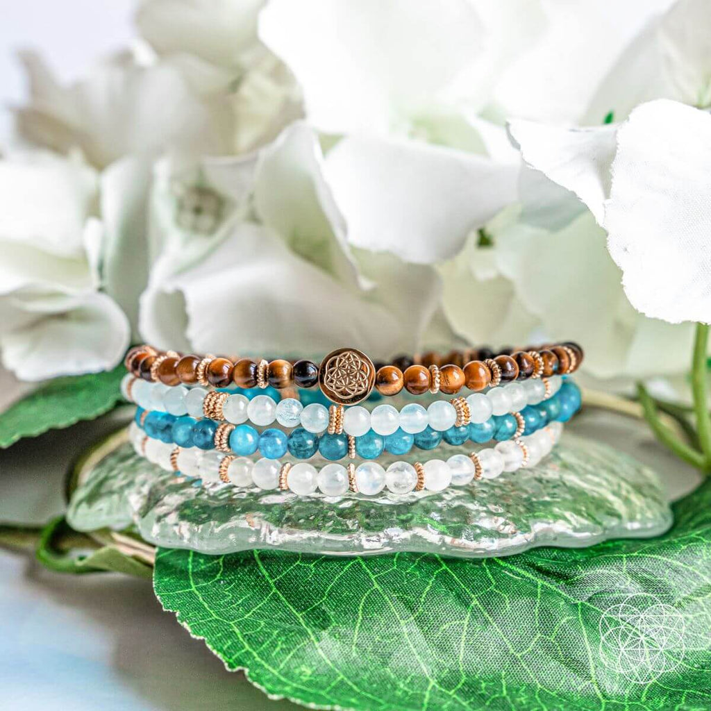 Stack of beaded bracelets on a decorative plate with flowers in the background