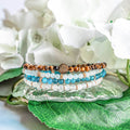 Stack of beaded bracelets on a decorative plate with flowers in the background