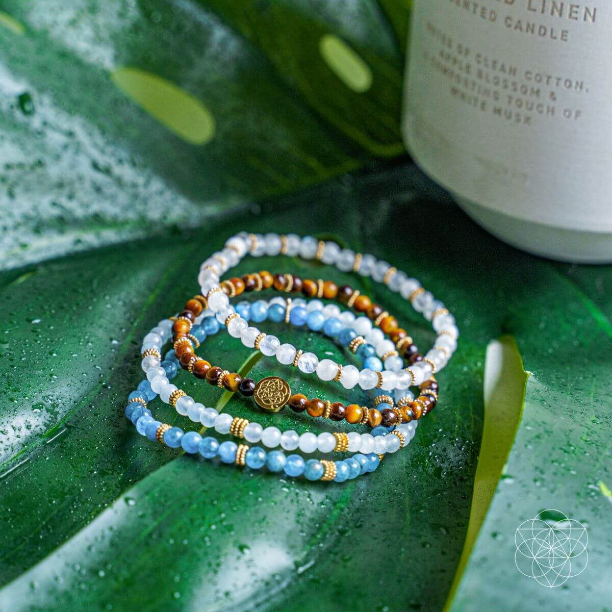 Stack of beaded bracelets on a green leaf with a candle in the background