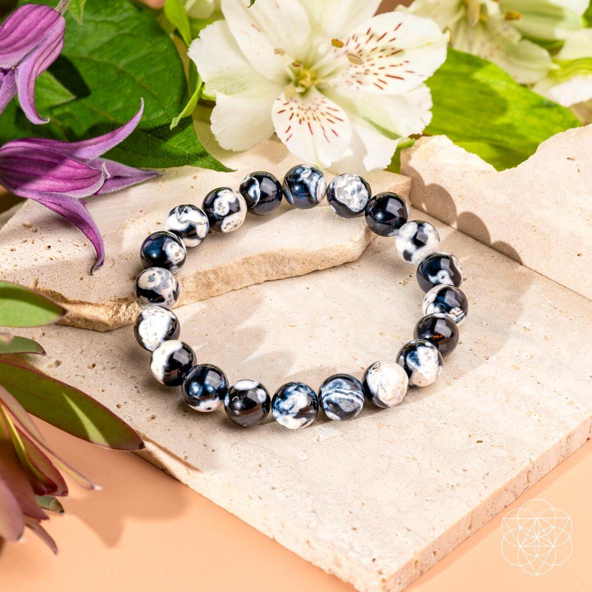 Black and silver beaded bracelet on a natural stone surface with flowers in the background