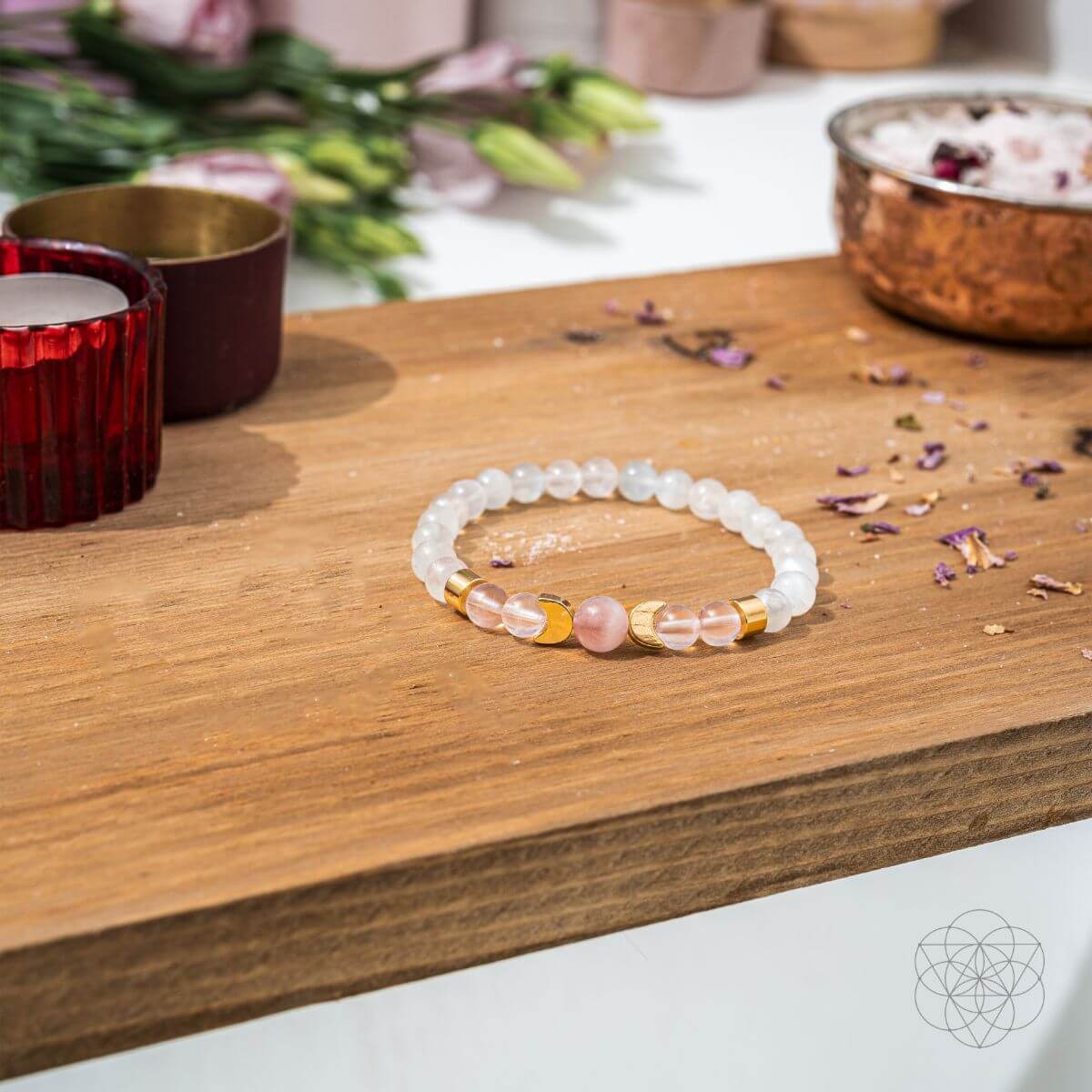 Beaded bracelet on a wooden surface with candles and flowers in the background
