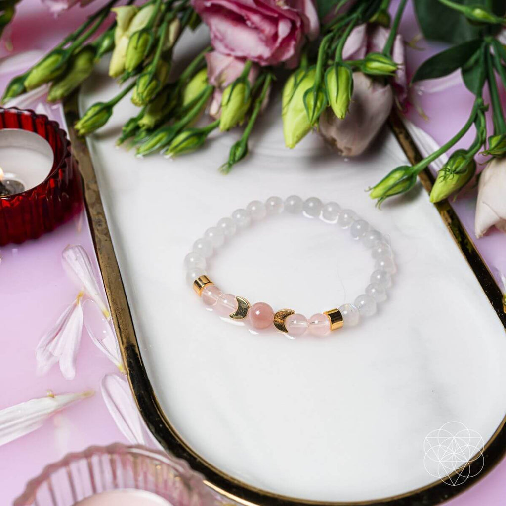 Bracelet with pink and gold beads on a white dish with flowers and a candle.