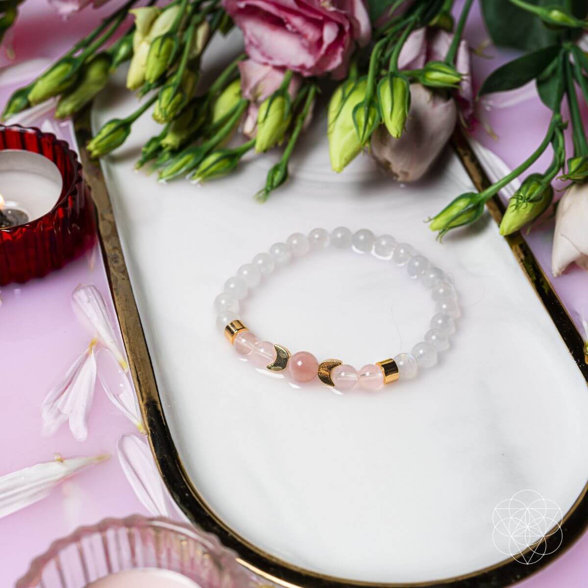 Bracelet with pink and gold beads on a white dish with flowers and a candle.