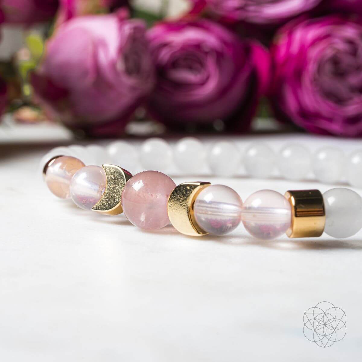 Bracelet with pink beads and gold accents on a white surface with purple flowers in the background