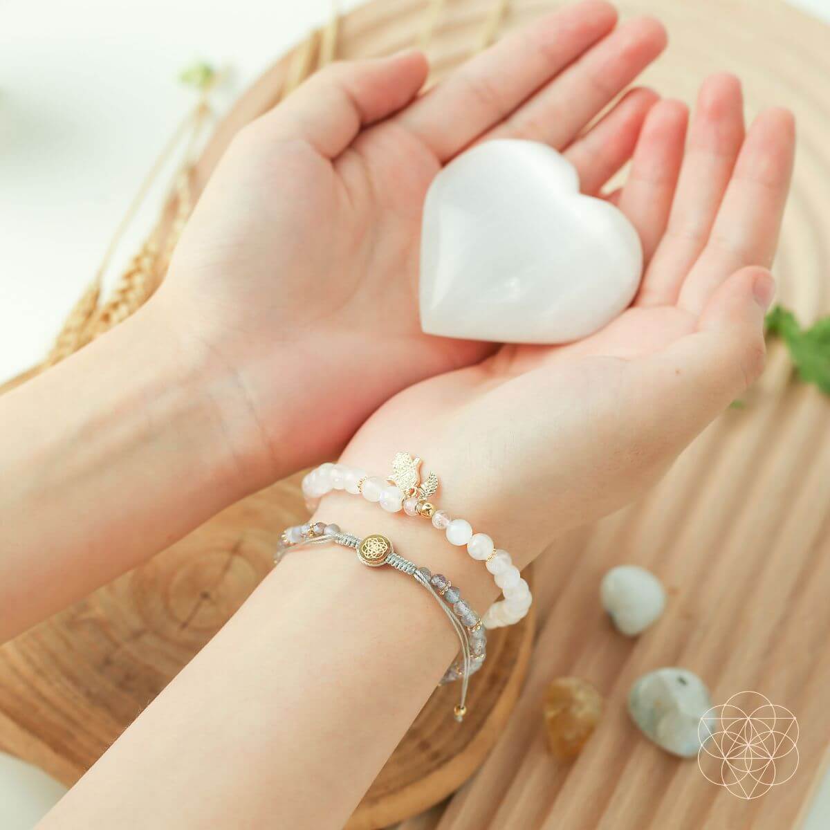 Heart-shaped stone held in hands with a background of stones and a circular emblem.