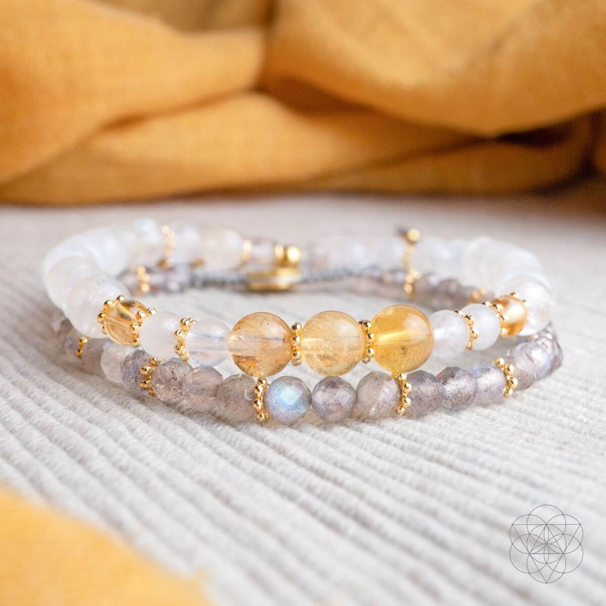 Stack of beaded bracelets with gold accents on a textured surface with a yellow fabric background