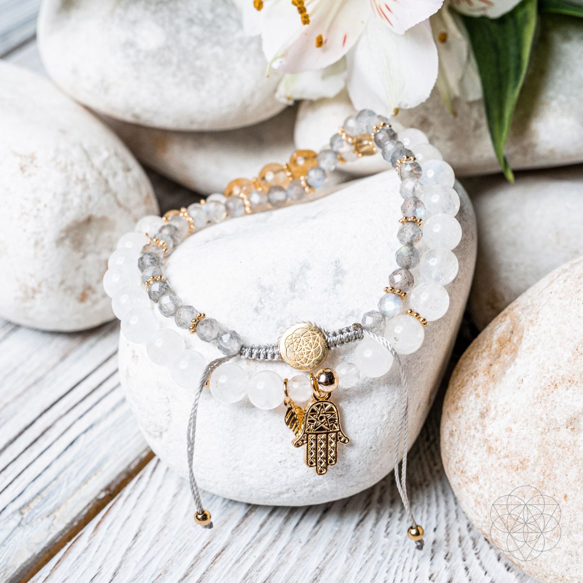 Bracelet with gemstones and a hamsa charm on a stone surface with flowers in the background
