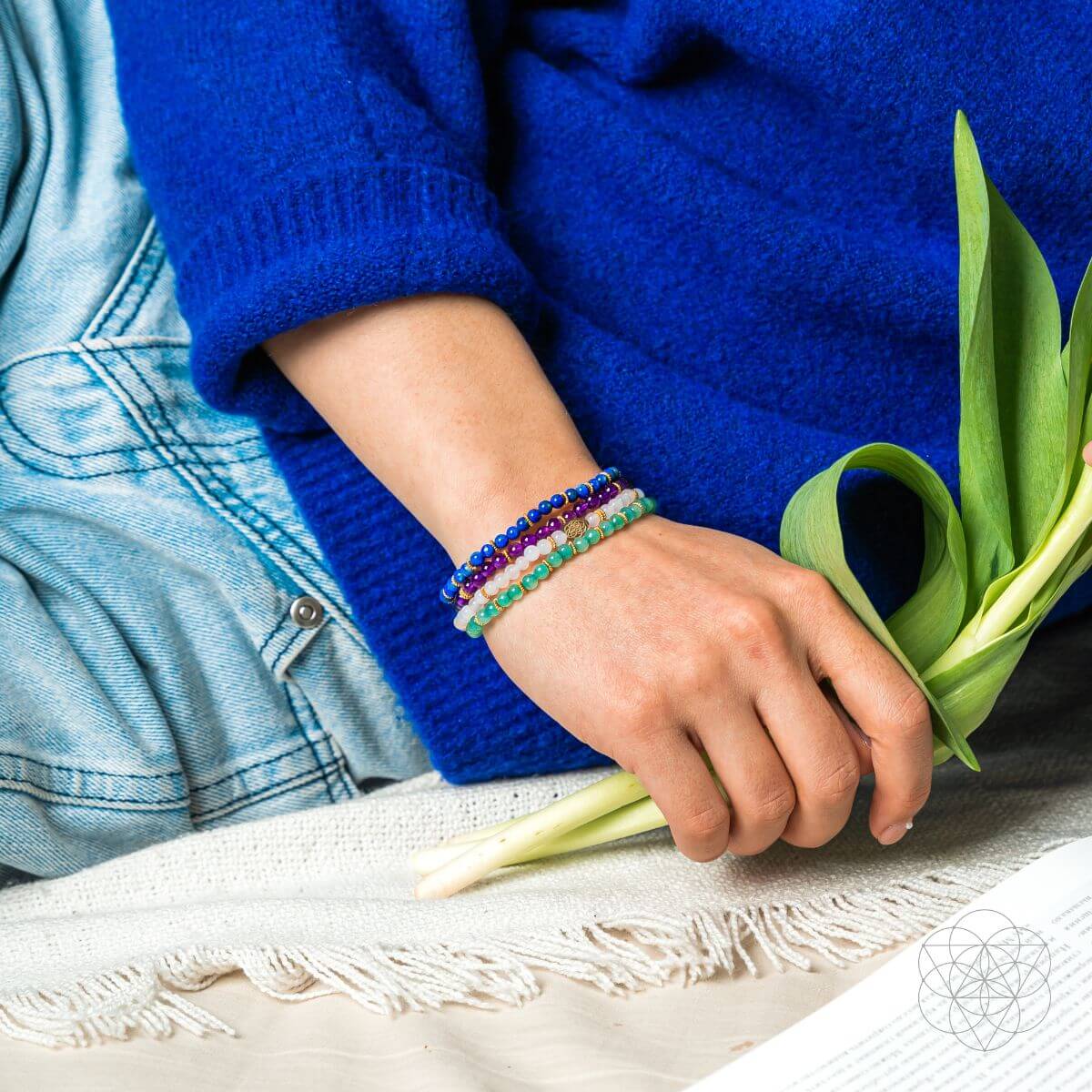 Person wearing colorful bracelets holding green tulip leaves on a textured surface